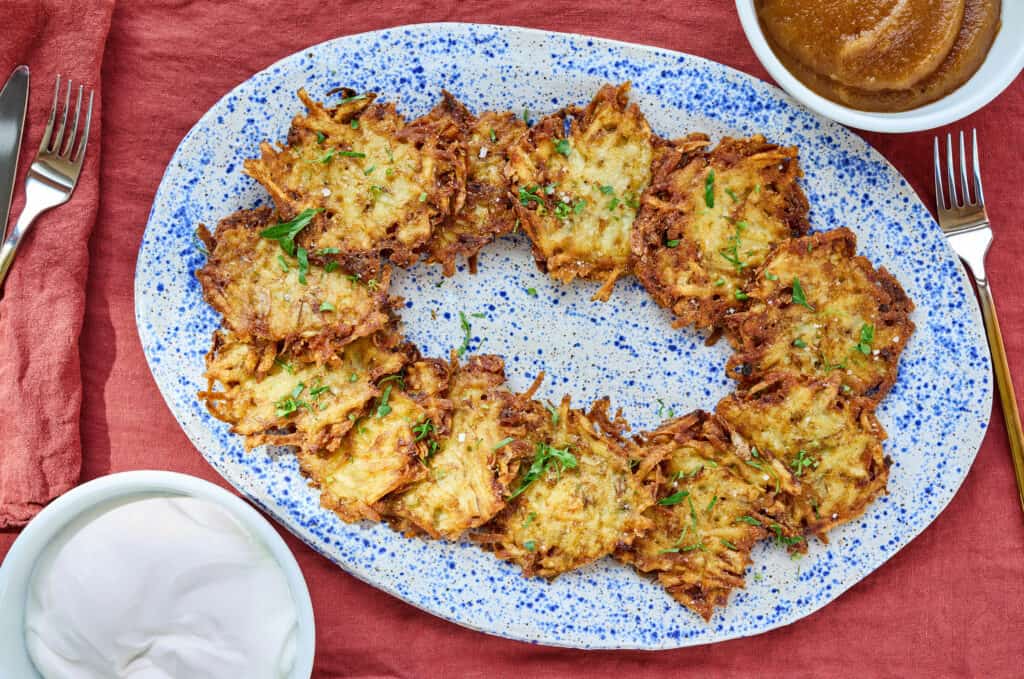 A platter of Potato Pancakes surrounded by bowls of sour cream and apple sauce
